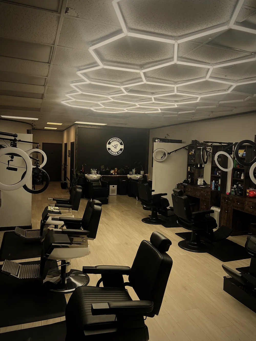 Barber stations and shampoo sinks under the lit Modesto Barber Co. logo